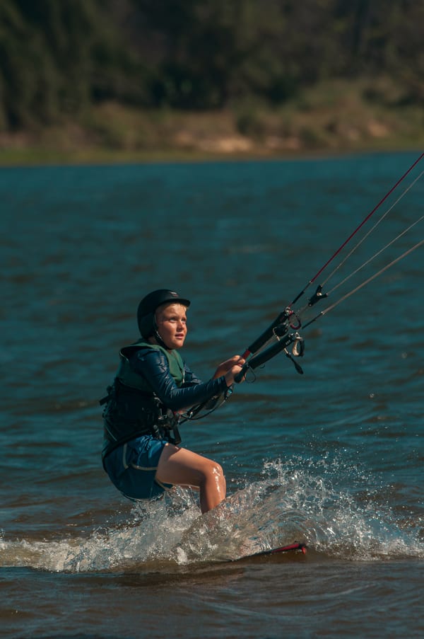 A young student riding alone across the lagoon, eyes on the kite